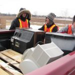 Workers unload pickup truck full of CRT monitors.